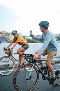 A young couple taking pictures with their mobile phones while on their bikes.