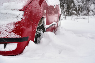 Red car parked in deep layer of snow after heavy snowstorm, detail to tire - only half wheel visible