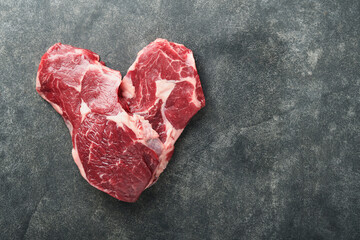 Raw beef steak. Marbled raw fresh Ribeye steak in heart shape with rosemary, salt and pepper on...