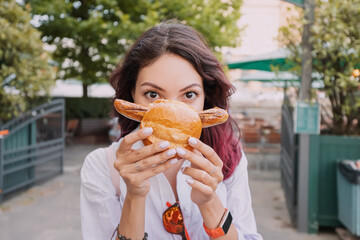 A happy girl eats an appetizing traditional German bratwurst hot dog with juicy sausage and...