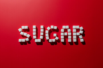 the word sugar is made up of sugar cubes on a red background. photo on the topic of the dangers of eating refined sugar