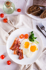 Homemade breakfast fried bacon and eggs, tomatoes and greens on a plate. Top and vertical view