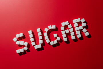 the word sugar is made up of sugar cubes on a red background. photo on the topic of the dangers of eating refined sugar