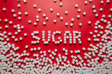 the word sugar is made up of sugar cubes on a red background. photo on the topic of the dangers of eating refined sugar