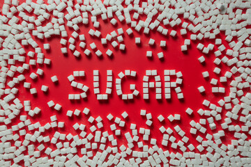 the word sugar is made up of sugar cubes on a red background. photo on the topic of the dangers of eating refined sugar