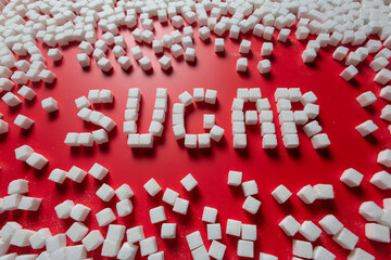 the word sugar is made up of sugar cubes on a red background. photo on the topic of the dangers of eating refined sugar