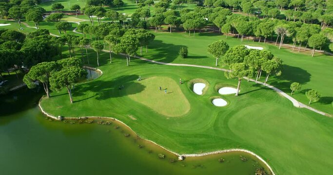 Aerial view of a green golf course on a sunny day. A view from a height of people playing golf. Golf course with a small pond and fountain.Aerial view of the golf course and golfers playing.