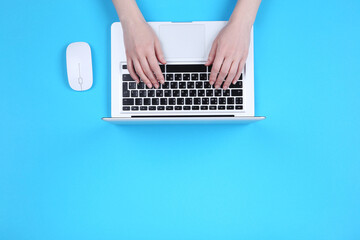 Fototapeta na wymiar Female hands typing on laptop keyboard with mouse on blue background