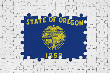 Oregon US state flag in frame of white puzzle pieces with missing central parts