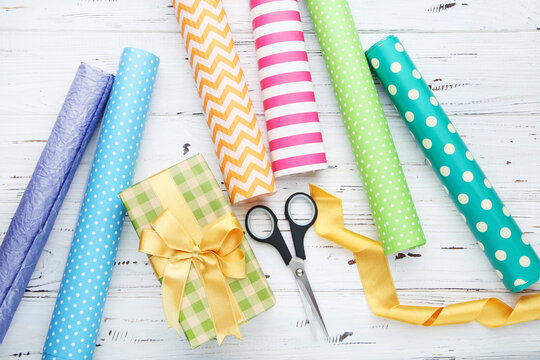 Rolls of craft papers with scissors and gift box on white wooden background