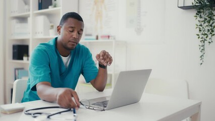 Portrait of African American doctor feeling exhausted at work, typing on laptop
