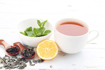 Cup of tea with dry tea, lemon and mint leafs on white wooden table