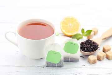 Obraz na płótnie Canvas Cup of tea with tea bags, sugar cubes and lemon on white wooden table