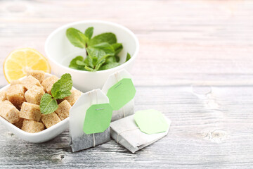 Tea bags with mint leafs, sugar cubes and lemon on wooden table
