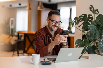 Shot of a young businessman using his laptop and phone at the working space. Happy business man...