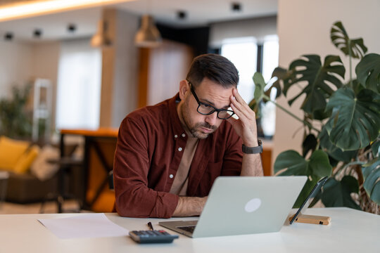 Contemplating Businessman In The Home Office Feeling Frustrated. Full Concentration On Work. Man Working On Laptop, Counting Profit While Sitting At The Desk At Home.