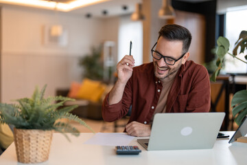 Obraz premium Young brown haired businessman looking joyful and proud of his work. Holding a pen in his hand, looking at a paper document and smiling.