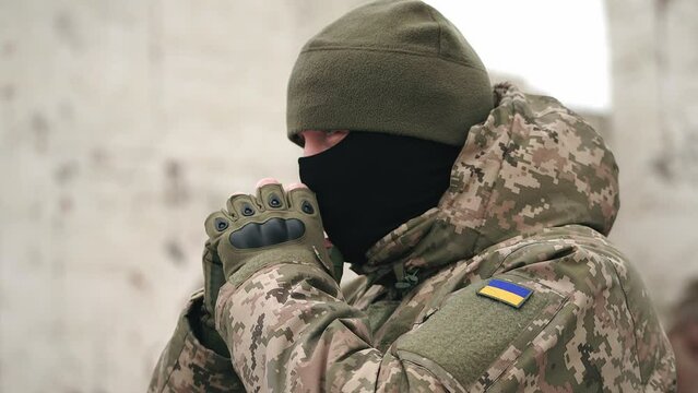 Ukrainian military man warms his hands with his breath on a cold winter morning. the officer at the post is warming up. war in winter winter military uniform. military service at sub-zero temperatures