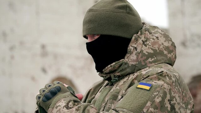 Ukrainian military man warms his hands with his breath on a cold winter morning. the officer at the post is warming up. war in winter winter military uniform. military service at sub-zero temperatures