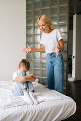 Obraz premium Vertical shot of sad crying little girl covering face with palm while angry young mother scolding, screaming and gesturing with hands at stubborn difficult little child daughter for bad behavior.