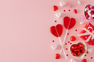 Valentine's Day sweet concept. Flat lay photo of two heart shaped lollipops, gift box, saucers with confectionery chocolate candies and marshmallow on pastel pink background with copy space.