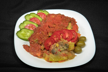 Potatoes and meat with vegetables in tomato sauce on a white plate