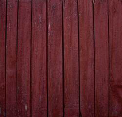 Background of old fence boards with red paint cracked from time to time. Close-up on weather-peeled boards with red paint. Texture of old painted wood.