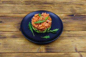 Salmon tartare with avocado and arugula on wooden table