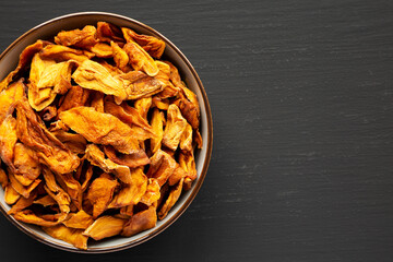 Delicious Organic Dried Mango Fruit in a Bowl on a black background, top view. Flat lay, overhead, from above. Space for text.