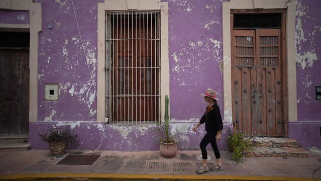 Pretty, mature, woman walking on a sidewalk along colorful buildings in Merida, Yucatan, Mexico.