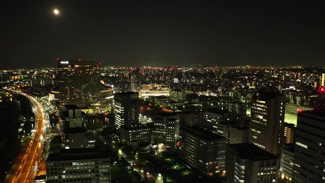 FUKUOKA, JAPAN - NOV 2022 : Aerial high angle view of Fukuoka City and full moon. Time lapse shot at night. View around Tenjin and Nakasu downtown area. Travel and urban city nightlife concept video.