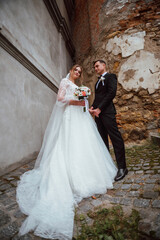 newlyweds in love on their wedding day pose for a photographer against the background of nature; he is in a dark classic jacket and she is in a white dress; a very happy and cheerful couple of people 