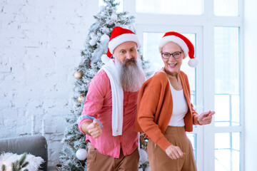 Obraz premium Christmas family grandmother and grandfather, elderly couple senior man and woman having fun near the Christmas tree, dancing and actively celebrating Christmas and New Year
