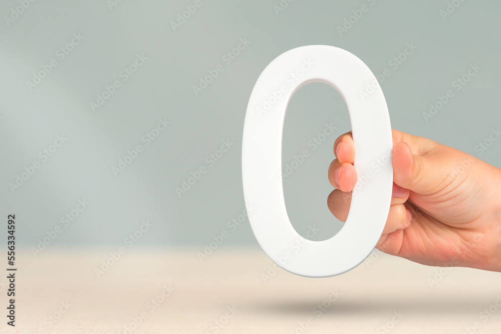 Aufkleber Numeral zero in hand. A hand holds a white number zero on a blurred background with copy space. Zero concept, 0 percent interest rate, minimum air emissions, cost or credit no increase.