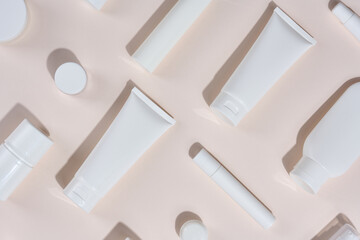 White plastic tubes, jars and other form of packaging for cosmetics on a beige background, top view.