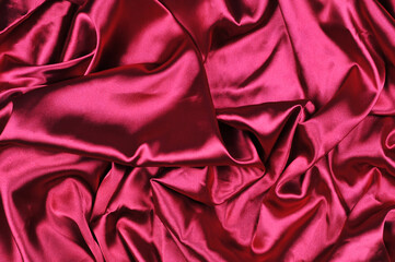 Magenta color silk waves texture background. Burgundy raspberry satin with color shine background. Top view.