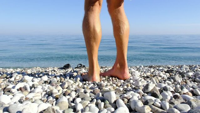 Man walks along pebble beach does feet massage. Acupuncture healthy lifestyle.