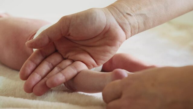 Hands of therapist rubs the small leg of infant. Masseur massaging little baby's foot. Happy infant girl doing baby massage by his mother at home. Newborn child about 2-5 months old.