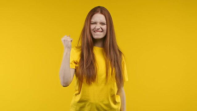 Pretty woman shows triumph yes yeah gesture of victory, achieved result, goals. Girl glad, happy, surprised excited happy lady on yellow background. Victory concept.