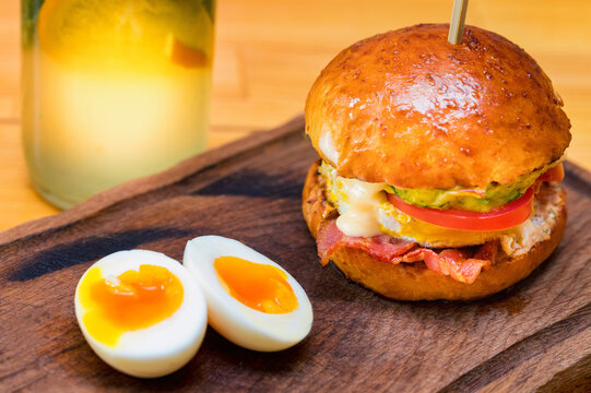 Close up tall tasty burger with cheese, tomatoes and omelet served on serving board