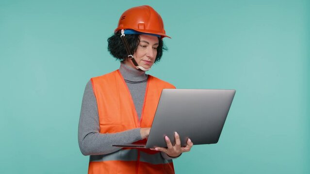 Female civil engineer, young female building architect use laptop on blue studio background. Reviewing future of real estate development planning. Wearing Safety helmet and vest, city construction 4K