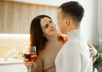 A young couple in love hugging and drinking red wine from glasses in a modern kitchen.