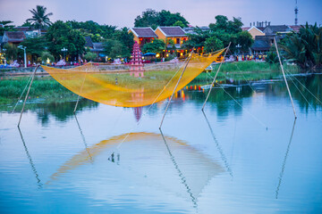 A fishing net suspended on poles over a river running past an historic village at Hoi An in Vietnam