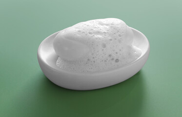Dish with soap bar and fluffy foam on green background