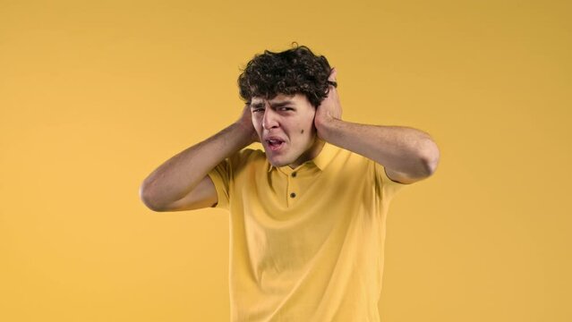 Annoyed curly man with shut ears on yellow background. Guy block annoying sounds, music, shouts or noise. Rolling eyes. Concept of conflict, problems.