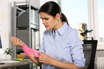 Fototapeta na wymiar Young woman applying medical bandage onto wrist in office