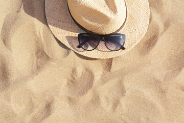 Hat with beautiful sunglasses on sand, top view. Space for text