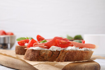 Tasty bruschettas with prosciutto, tomatoes and cheese on wooden board, closeup