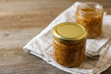 Jars of whole grain mustard on wooden table. Space for text