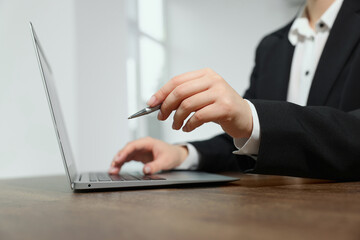 Woman with pen working on laptop at wooden table, closeup. Electronic document management